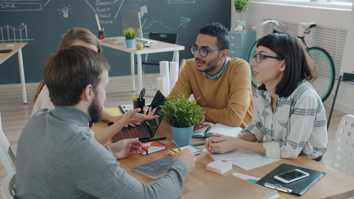 A small team collaborating around a table with laptops in an office