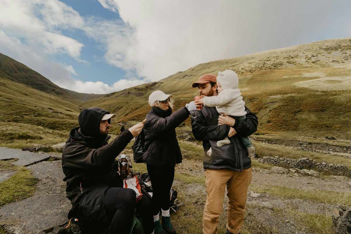 A family with a young child sharing a drink together on a mountain hike