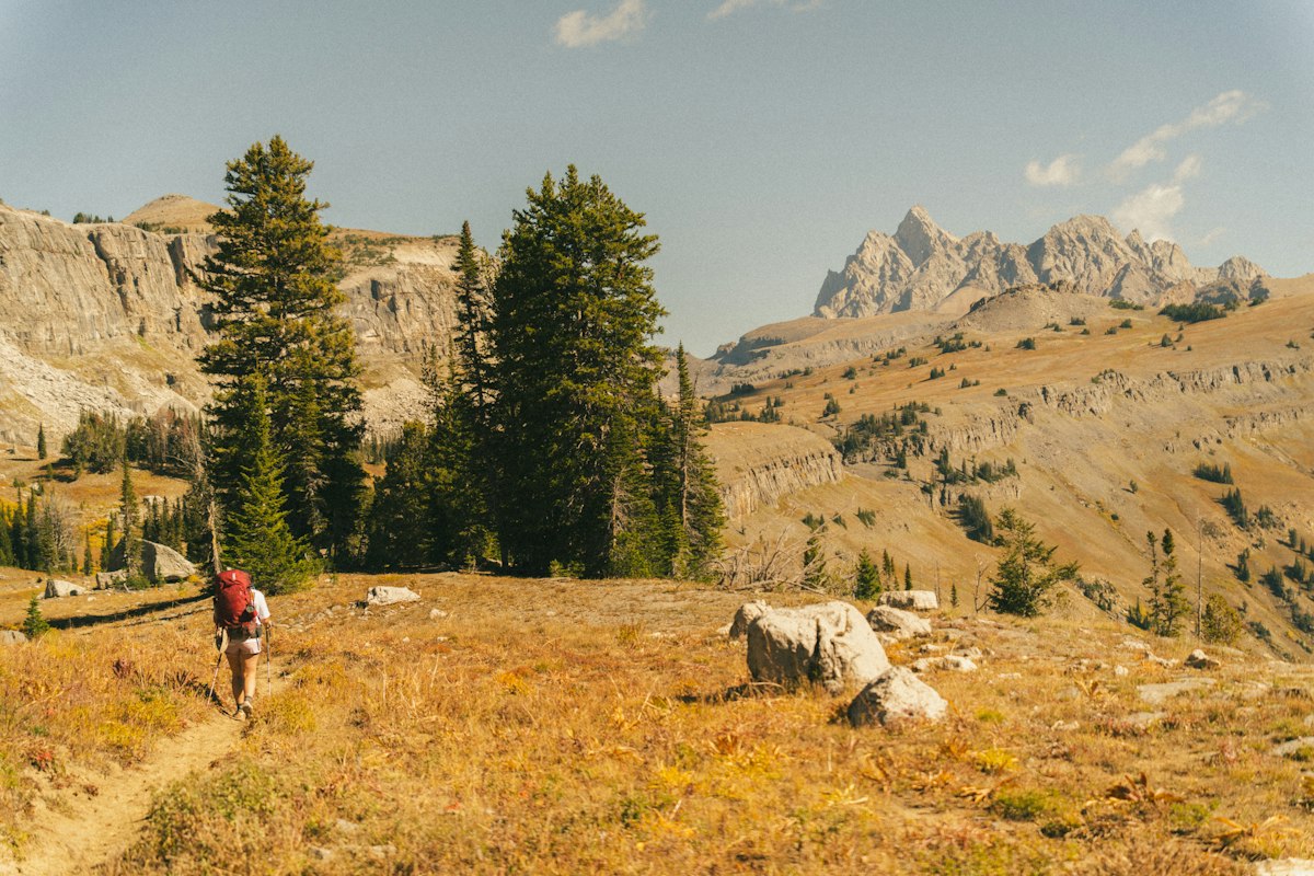 A hiker with a red backpack walking a mountain trail alone