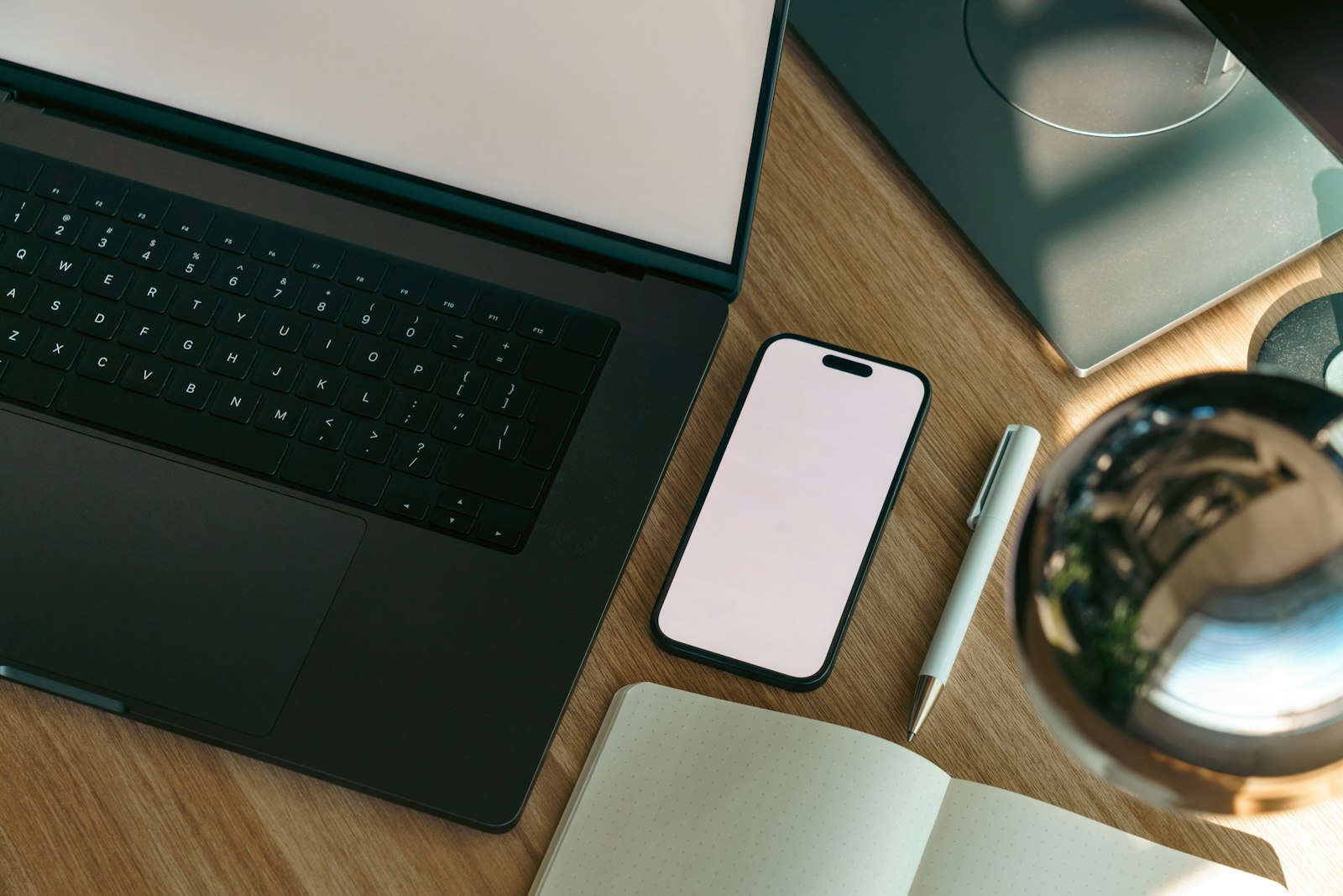 A laptop, phone, notebook, and pen laid out on a desk