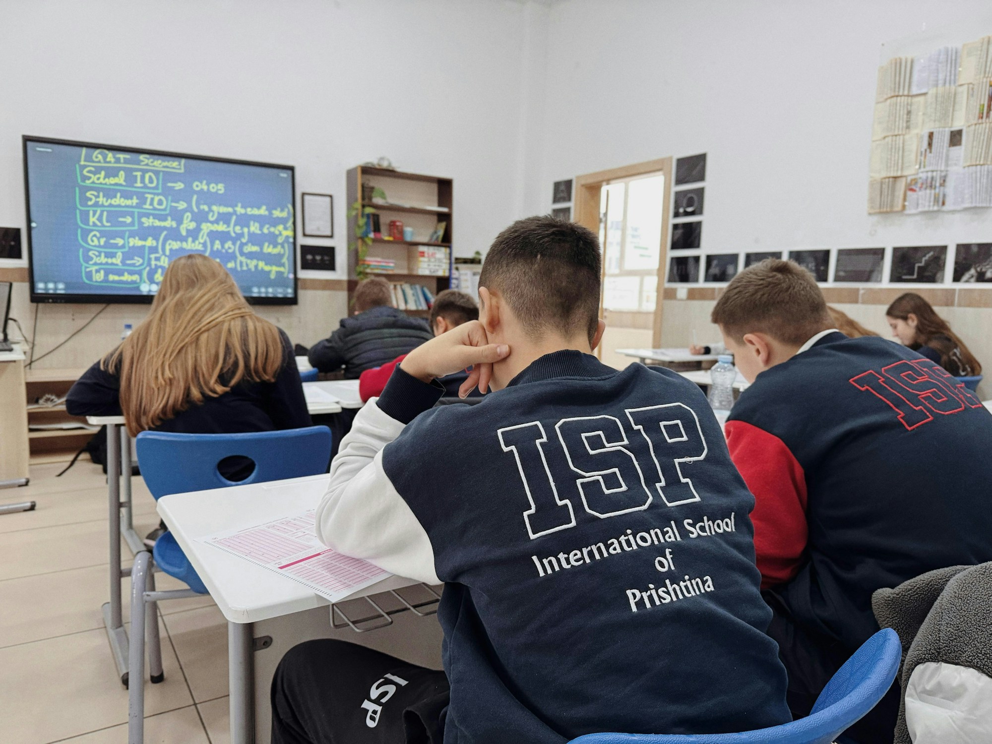 Highschool students at their desks, in a real classroom, with the lesson on screen