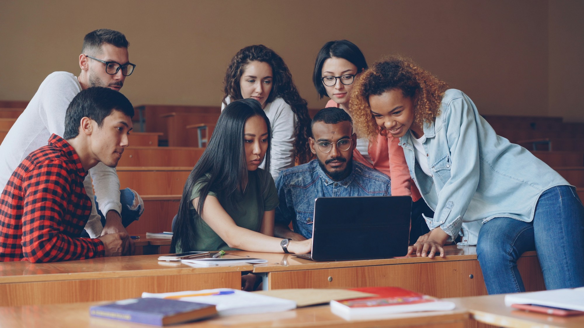 A group of university students collaborating around a laptop in a lecture hall
