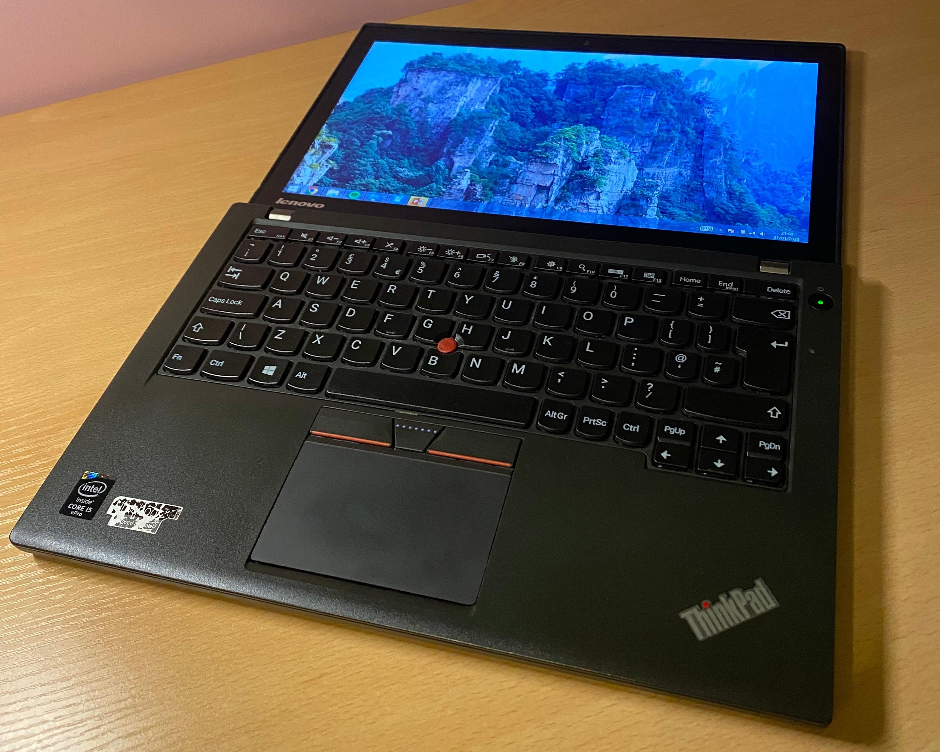 A Lenovo ThinkPad X250 laptop, open, on a wooden desk