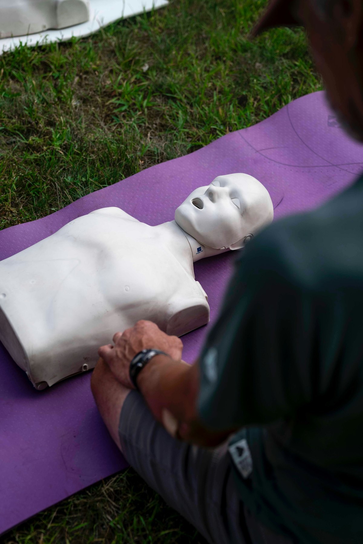 A person practicing CPR chest compressions on a training dummy outdoors